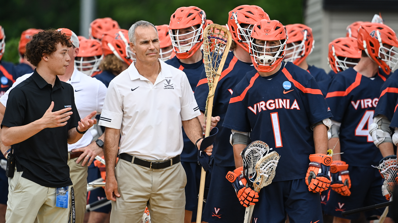 Virginia coach Lars Tiffany with his wooden lacrosse stick leading his team into a game at Johns Hopkins